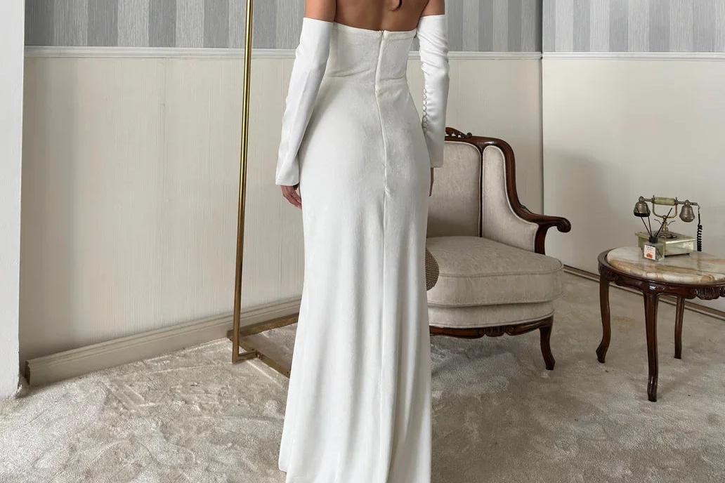 Woman in a white dress standing in a stylish room with striped walls and a chandelier.